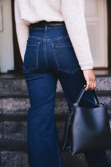 En kvinde i et par mørkeblå jeans, hun ses bagfra fra livet og ned. Hun har en sort taske i hånden
